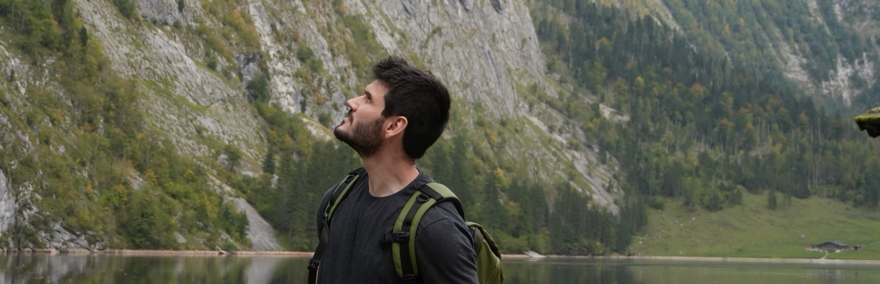Vitor Xavier looking up at a mountain ridge beside an alpine lake